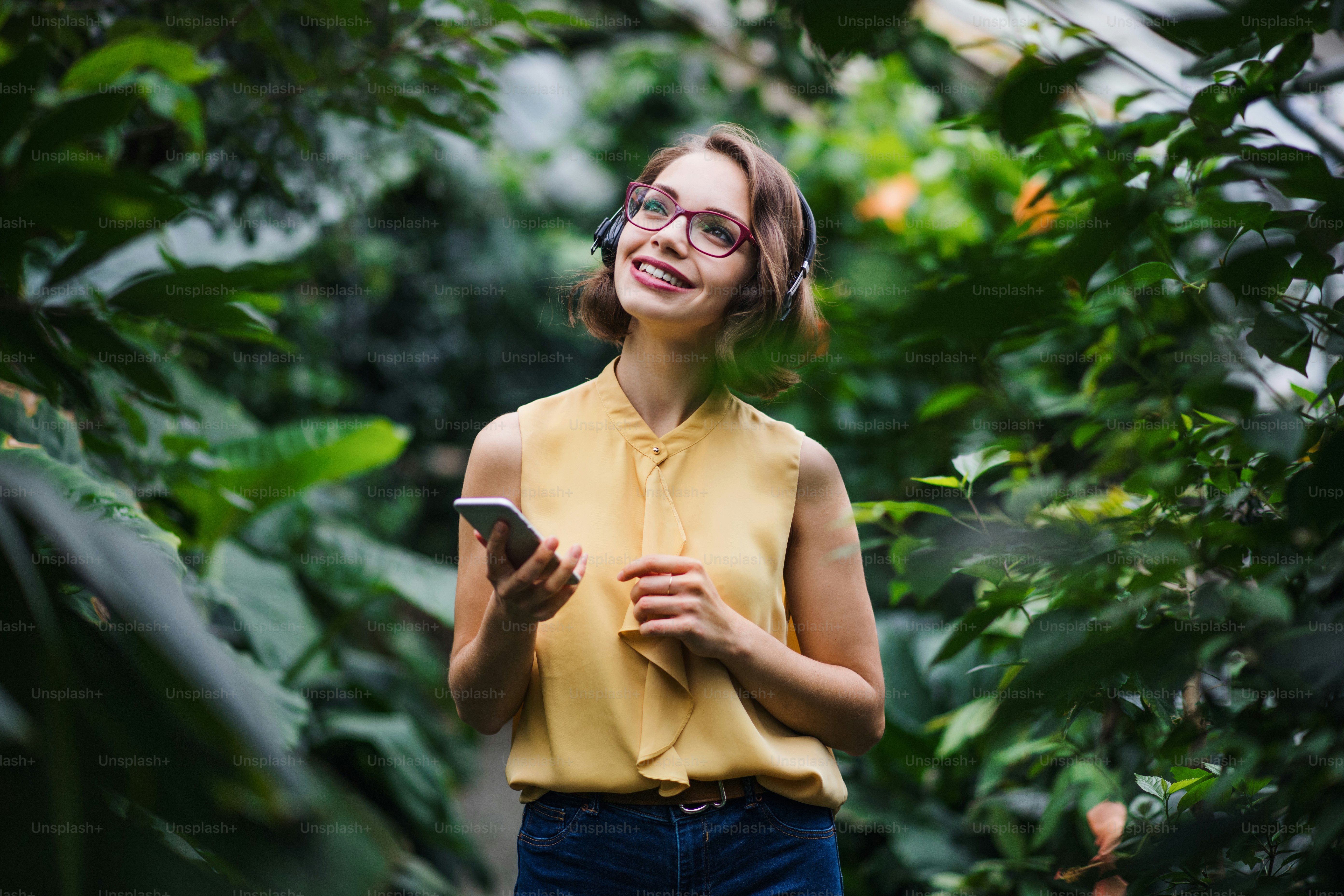 Young woman with smartpone standing in greenhouse in botanical garden. Copy space