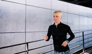 A young sportswoman doing exercise outdoors in city, running.