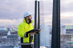 Mature man engineer standing on construction site, holding blueprints.