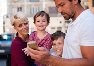A young family with two small children standing outdoors in town, using smartphone.