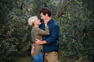 A young affectionate couple standing outdoors in olive orchard, hugging.