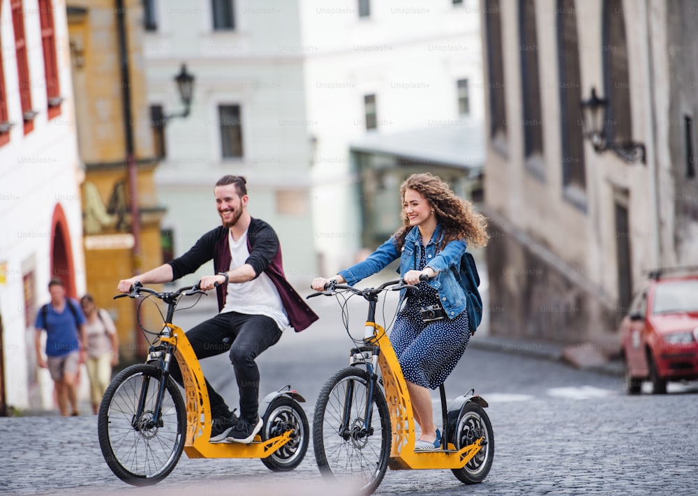 Joven pareja de turistas viajeros con scooters eléctricos en una pequeña ciudad, haciendo turismo.