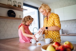 Ein glückliches süßes kleines Mädchen mit Mutter drinnen in der Küche zu Hause, Tee trinkend.