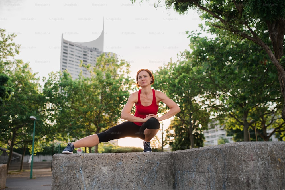 A young woman doing exercise outdoors in city at sunset, stretching.