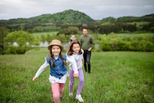 Happy family with two small daughters running outdoors in spring nature, holding hands.