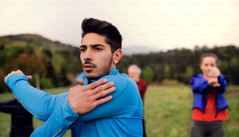 A portrait of young man with large group of people doing exercise in nature, stretching.