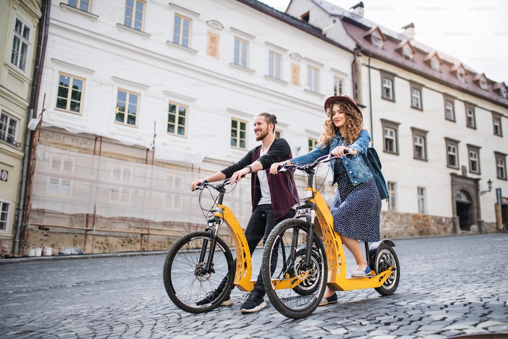 Joven pareja de turistas viajeros con scooters eléctricos en una pequeña ciudad, haciendo turismo.