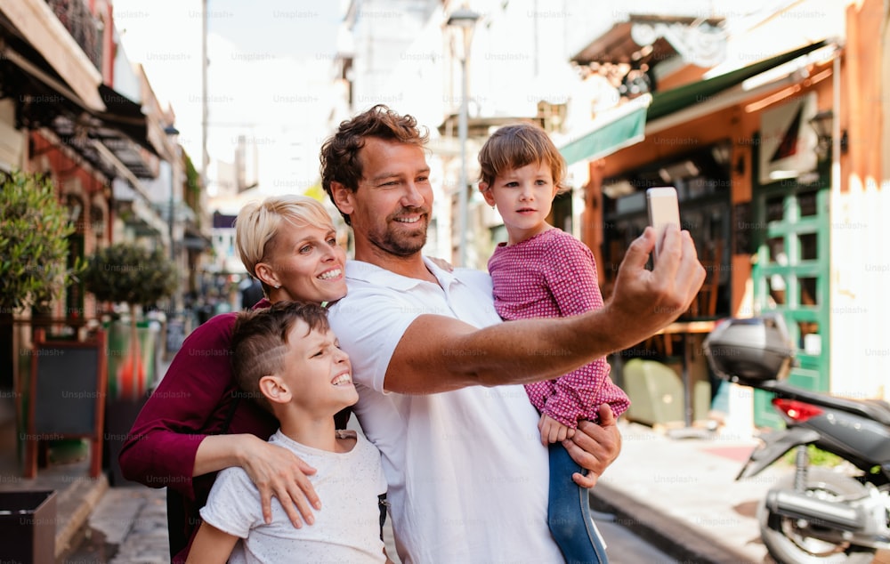 Eine junge Familie mit zwei kleinen Kindern steht draußen in der Stadt und macht Selfies mit Smartphone.