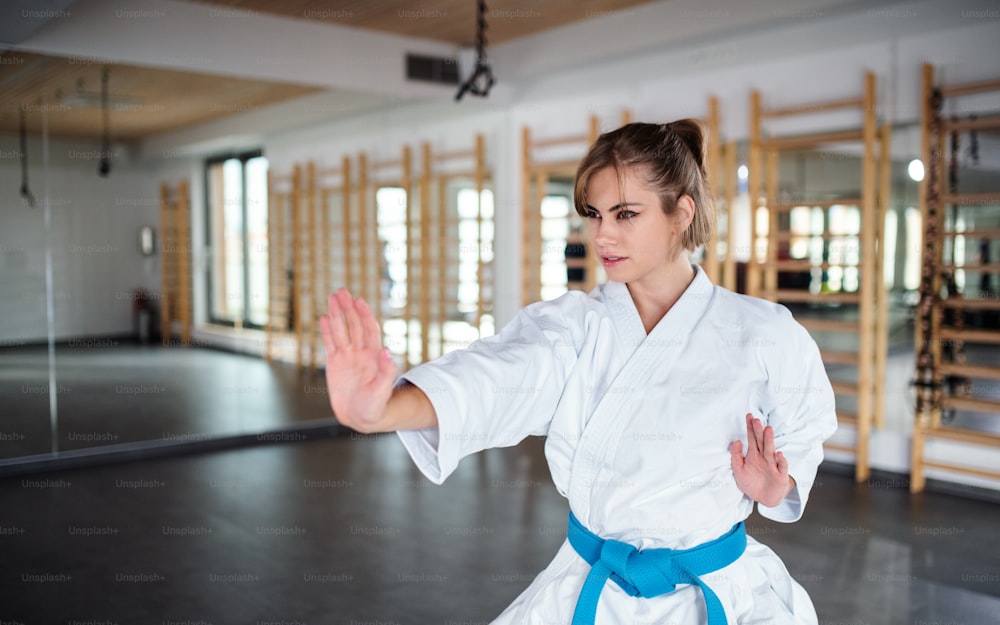 An attractive young woman practising karate indoors in gym.