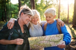 Senior women friends on a walk outdoors in forest, using map and binoculars.