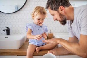Padre maduro con una niña pequeña en el interior del baño, pintando uñas.