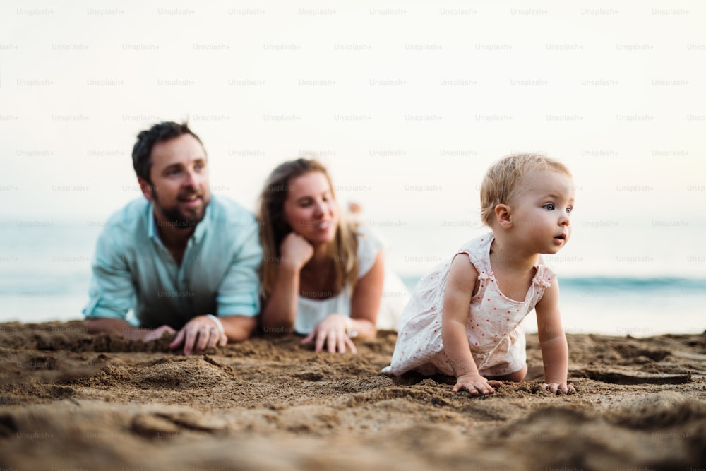 A family with a toddler girl lying on sand beach on summer holiday, playing.
