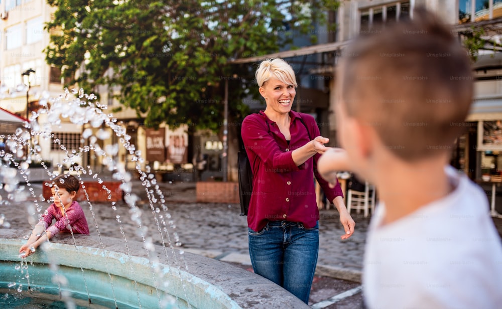 Young mother with two small children having fun by the fountain outdoors in town.