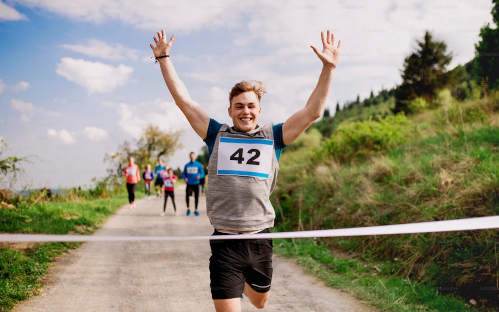 Um jovem corredor cruzando a linha de chegada em uma competição de corrida na natureza, braços levantados.