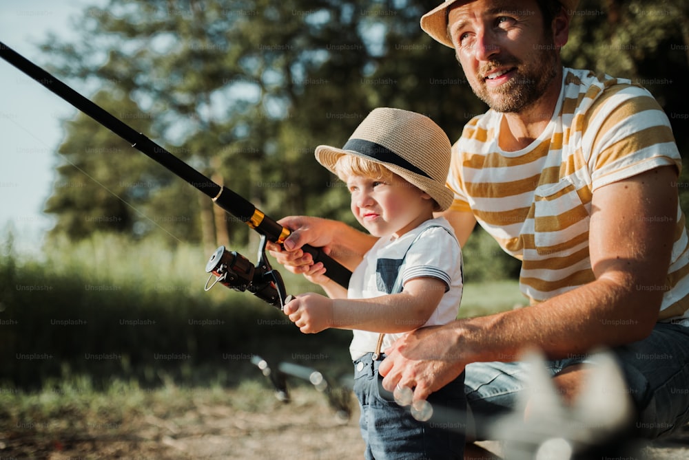Un padre maduro con un hijo pequeño pescando al aire libre junto a un río o un lago.