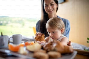 Giovane donna con la figlia piccola che mangia la colazione al chiuso, fine settimana in una casa container in campagna.