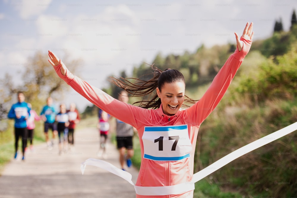 Una joven corredora cruza la línea de meta en una competición de carreras en la naturaleza, con los brazos en alto.