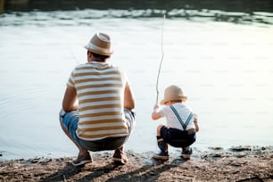 Una vista trasera de un padre maduro con un hijo pequeño al aire libre pescando junto a un río o un lago.