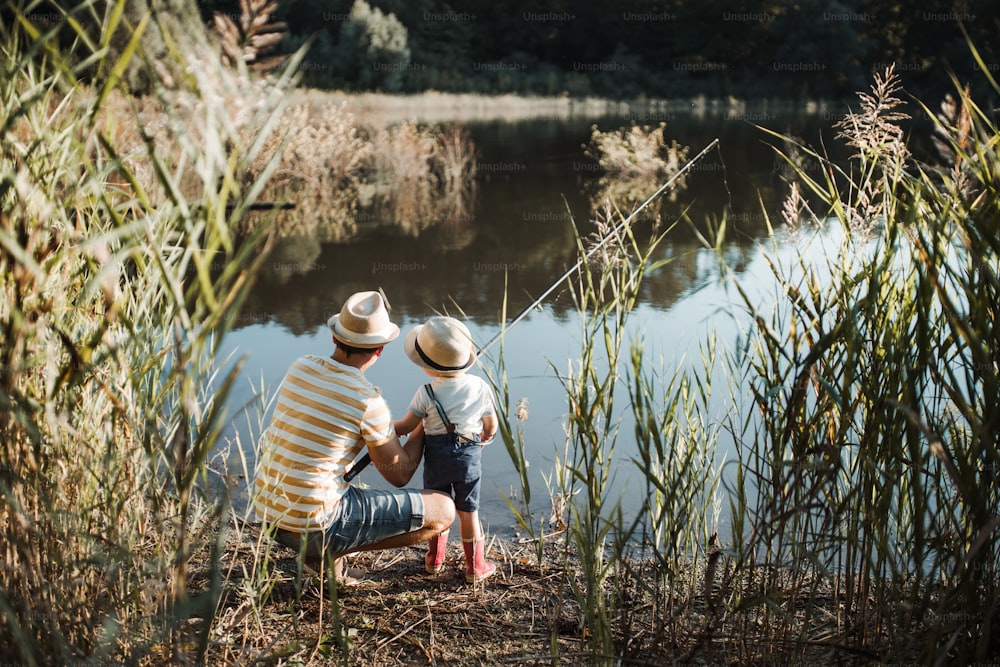 Una vista trasera de un padre maduro con un hijo pequeño al aire libre pescando junto a un río o un lago.