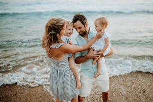 Uma família jovem e feliz com duas crianças pequenas em pé na praia nas férias de verão.