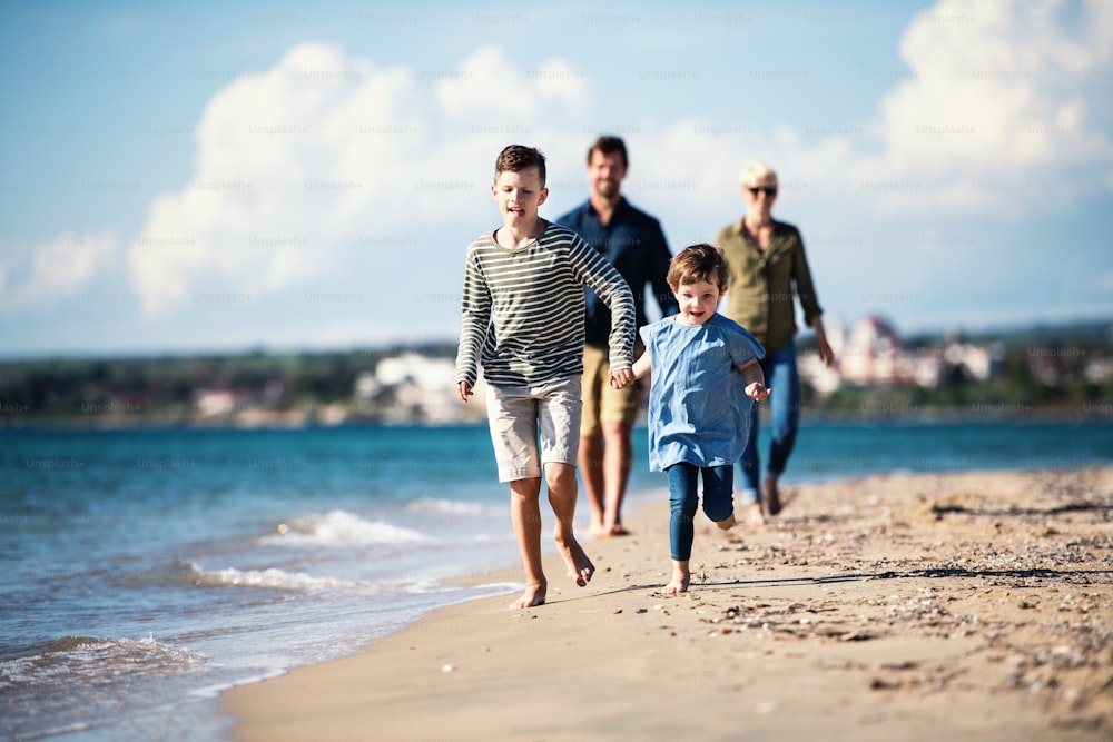 Young family with two small children walking barefoot outdoors on beach.