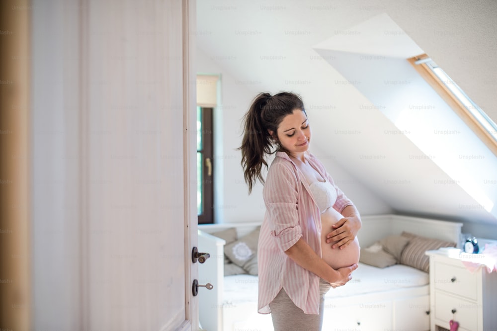Portrait of happy pregnant woman indoors at home, touching her belly. Copy space.