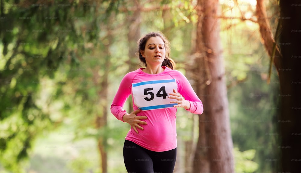 Hermosa mujer embarazada que corre una competencia de carreras en la naturaleza.