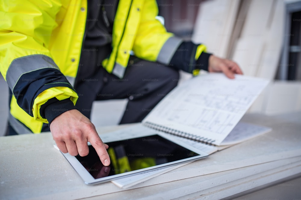 Unrecognizable man engineer standing on construction site, holding tablet with blueprints.