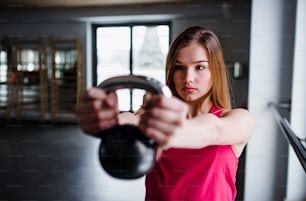 A portrait of a beautiful young girl or woman doing exercise with a kettlebell in a gym.