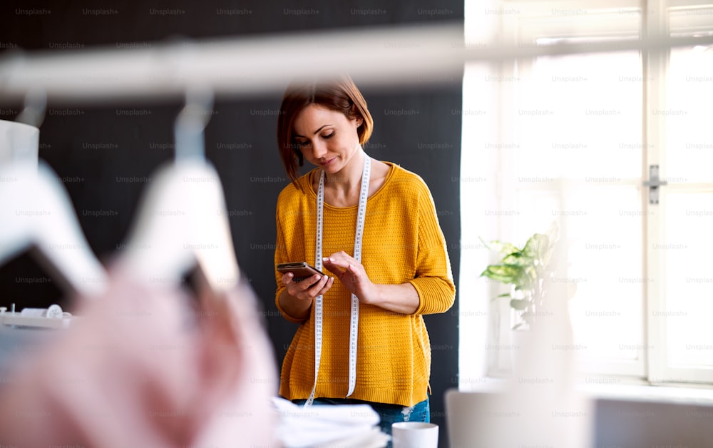 Young creative woman in a studio, using smartphone. A startup of small tailoring business. Copy space.