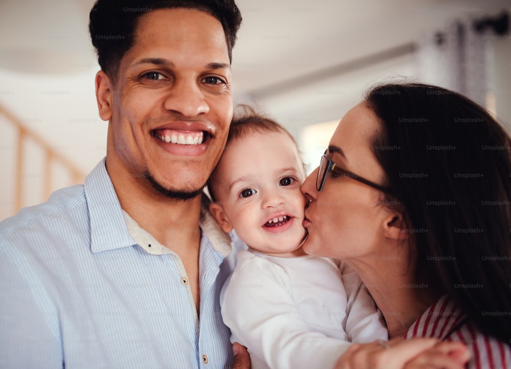 A portrait of young family with small toddler son indoors at home, kissing.