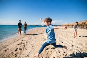 A cheerful small girl with family running outdoors on sand beach, having fun.