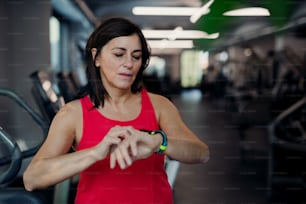 Una mujer mayor contenta con reloj inteligente en el gimnasio descansando después de hacer ejercicio, comprobando el tiempo. Espacio de copia.