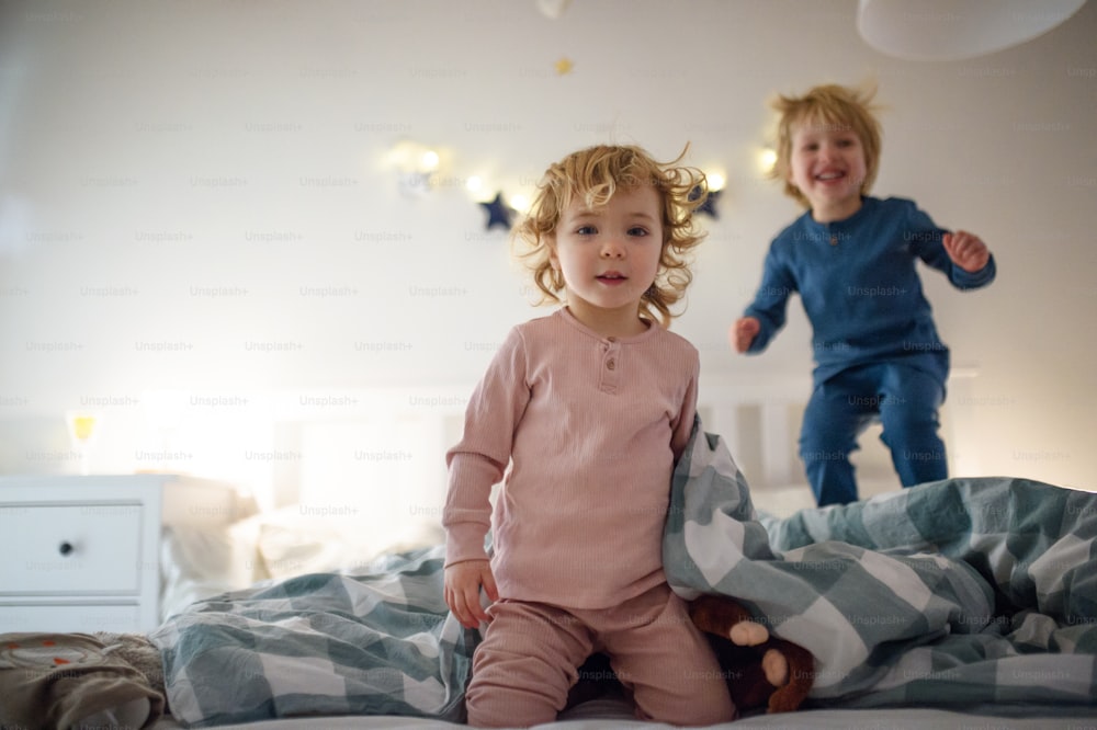 2人の小さな笑い声の子供が家の屋内でベッドに飛び乗って楽しんでいます。