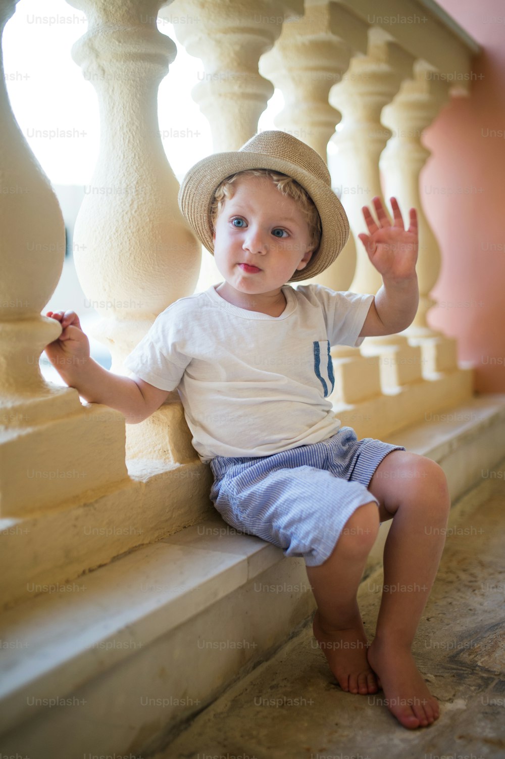 A portrait of small toddler boy sitting in front of concrete railing or balustrade on summer holiday.
