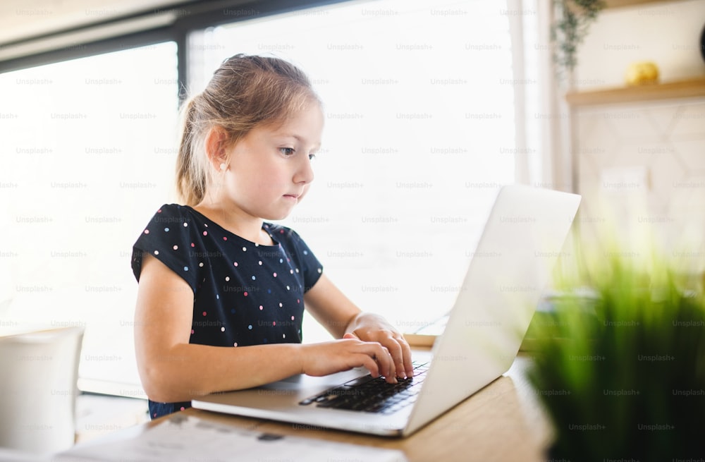 Menina pequena sentada à mesa e usando laptop dentro de casa, Corona vírus e conceito de quarentena.