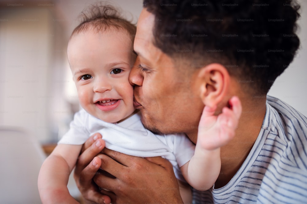 Ein Porträt von fröhlichem Vater und kleinem kleinen Sohn drinnen zu Hause, küssen.