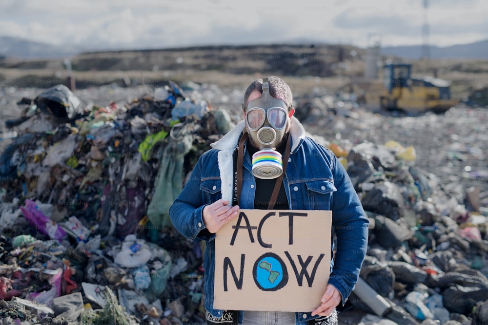 Front view of man with gas mask and placard poster on landfill, environmental concept.