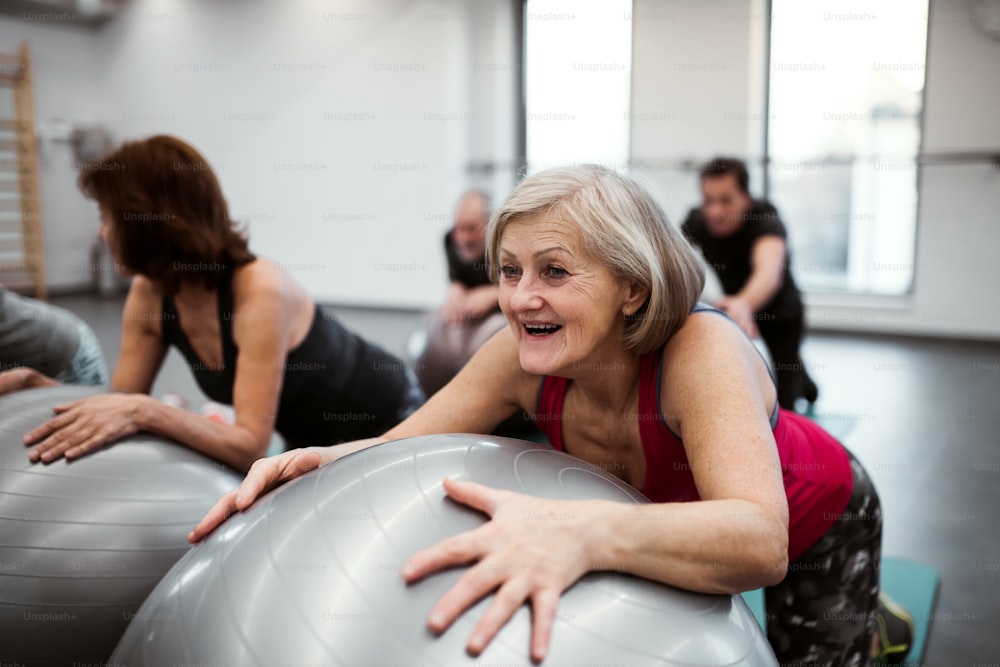 Eine Gruppe fröhlicher weiblicher Senioren im Fitnessstudio, die an fitten Bällen trainieren.
