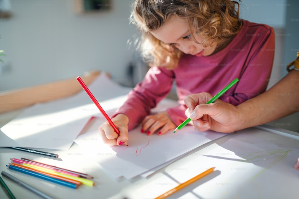 A cute small girl with unrecognizable mother in bedroom indoors at home, drawing pictures.