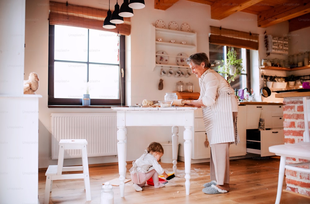 A senior great grandmother with small toddler grandchild making cakes at home.