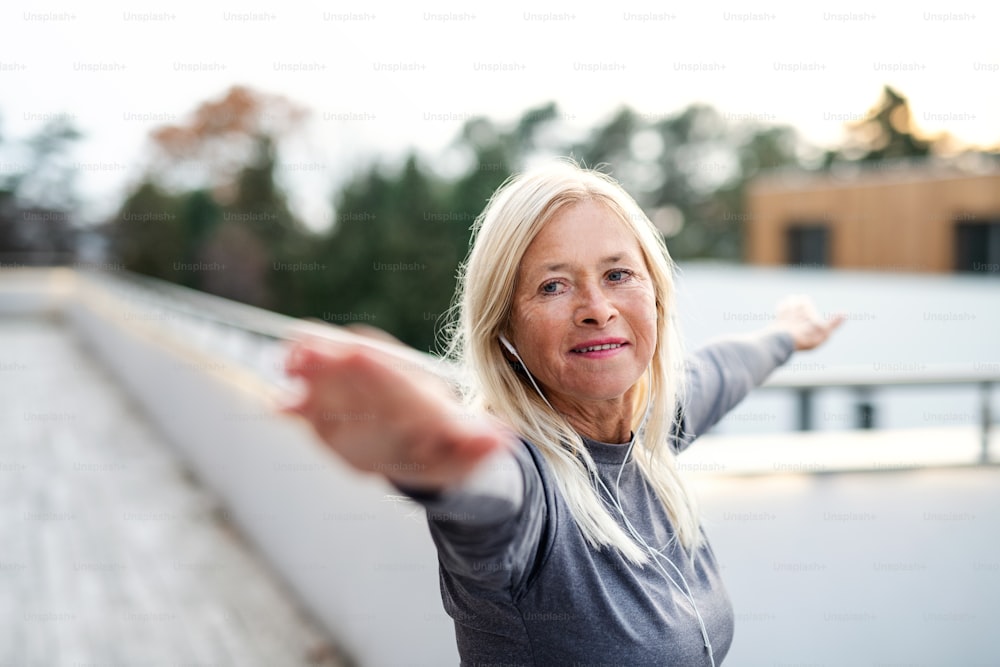 Une femme âgée avec des écouteurs à l’extérieur faisant de l’exercice sur la terrasse.