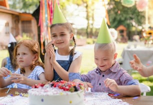 Down syndrome child with friends on birthday party outdoors in garden in summer.