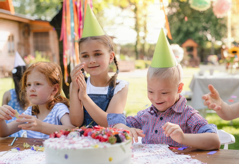 Síndrome de Down criança com amigos na festa de aniversário ao ar livre no jardim no verão.