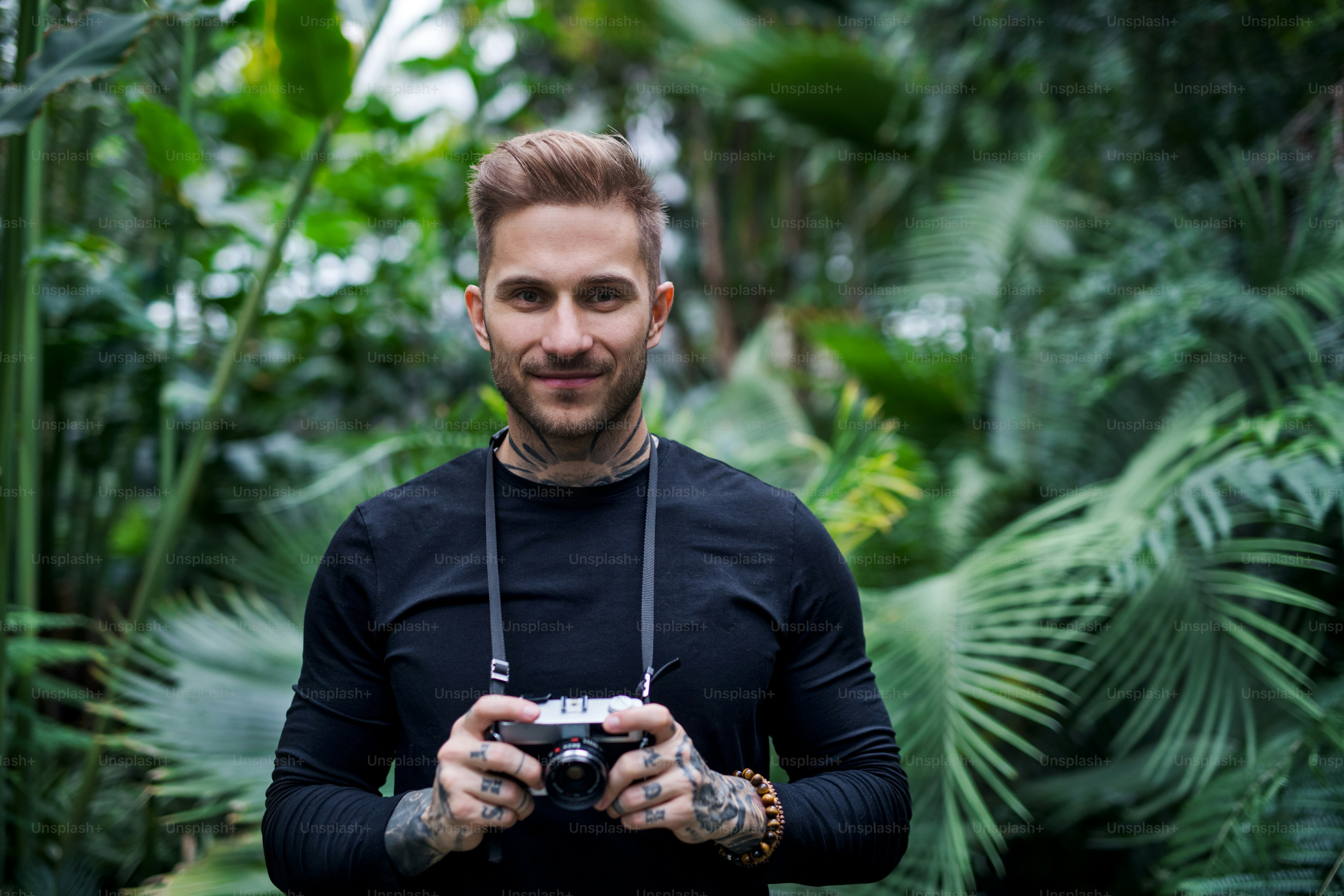 Eine Vorderansicht eines jungen Mannes mit Kamera im botanischen Garten.