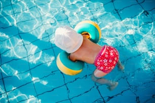 A top view of small child with armbands in swimming pool on summer holiday.