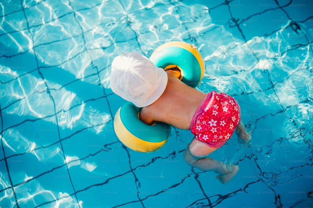 Uma vista superior da criança pequena com braçadeiras na piscina nas férias de verão.