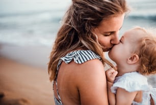 A close-up of young mother with a toddler girl on beach on summer holiday, kissing.