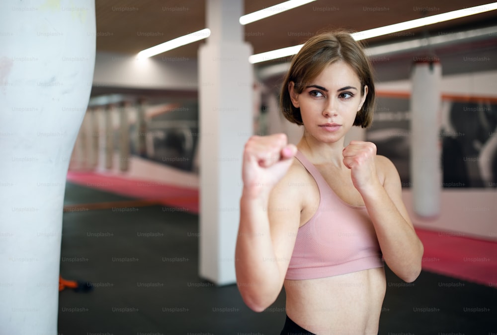 Una vista frontal de una mujer joven practicando karate en el interior del gimnasio.