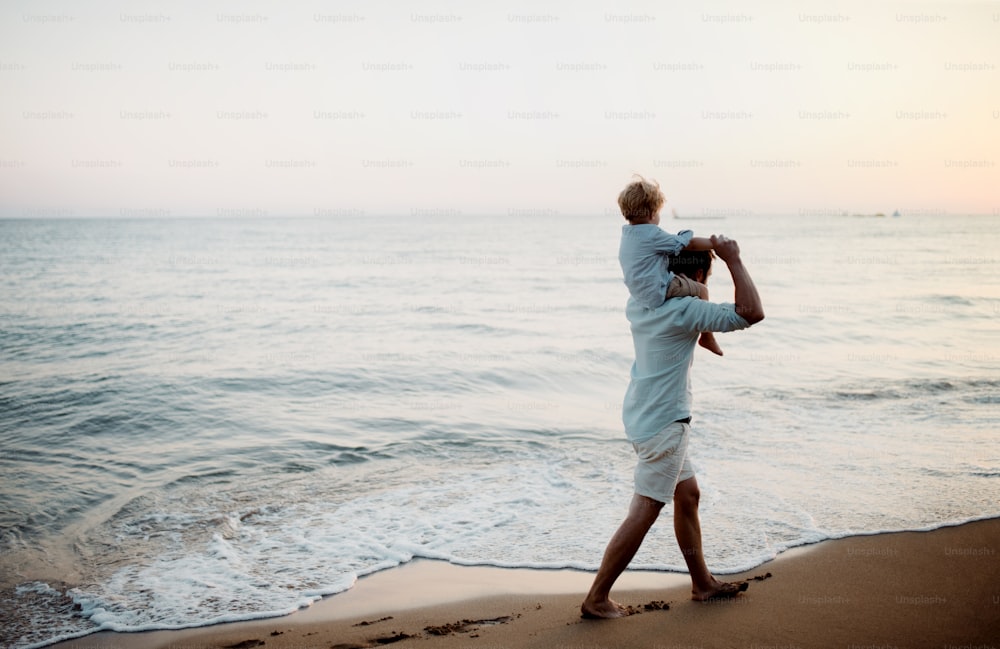 Padre maduro con un niño pequeño caminando por la playa en vacaciones de verano, divirtiéndose.